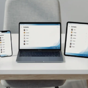 Smartphone, laptop en tablet op wit bureau met gesynchroniseerde contactenlijst in Microsoft 365-werkomgeving.