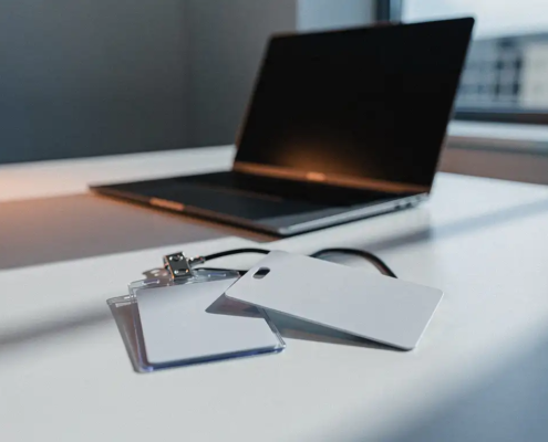 Toegangspas en kantoorsleutelkaart op wit bureau, één kaart doorkruist door schaduw, laptop op achtergrond in grijsblauwe tinten.