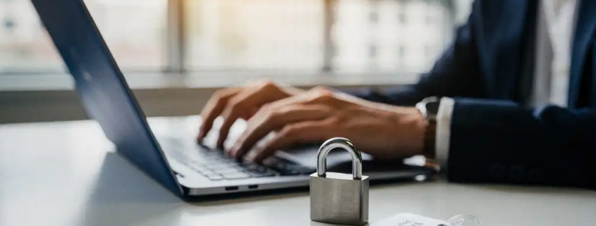 Kantoormedewerker bij laptop met fysiek hangslot en toegangspas op toetsenbord, symboliseert digitale beveiliging op de werkvloer.