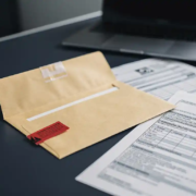 Opengevallen manillaenvelop met rode waarschuwingstag op modern bureau, omringd door officiële documenten en gedeeltelijk zichtbare laptop.