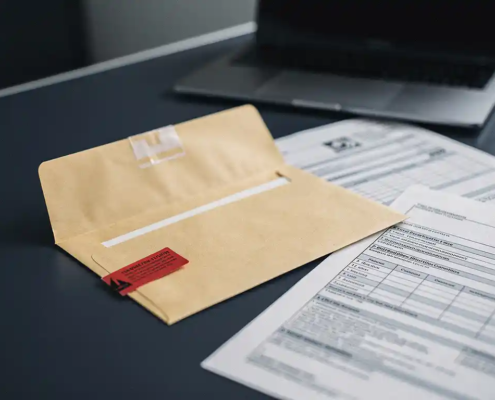 Opengevallen manillaenvelop met rode waarschuwingstag op modern bureau, omringd door officiële documenten en gedeeltelijk zichtbare laptop.