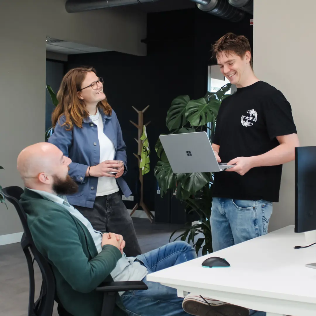 Twee collega’s van Puur ICT staan bij het bureau van een andere collega en zijn met elkaar in gesprek.